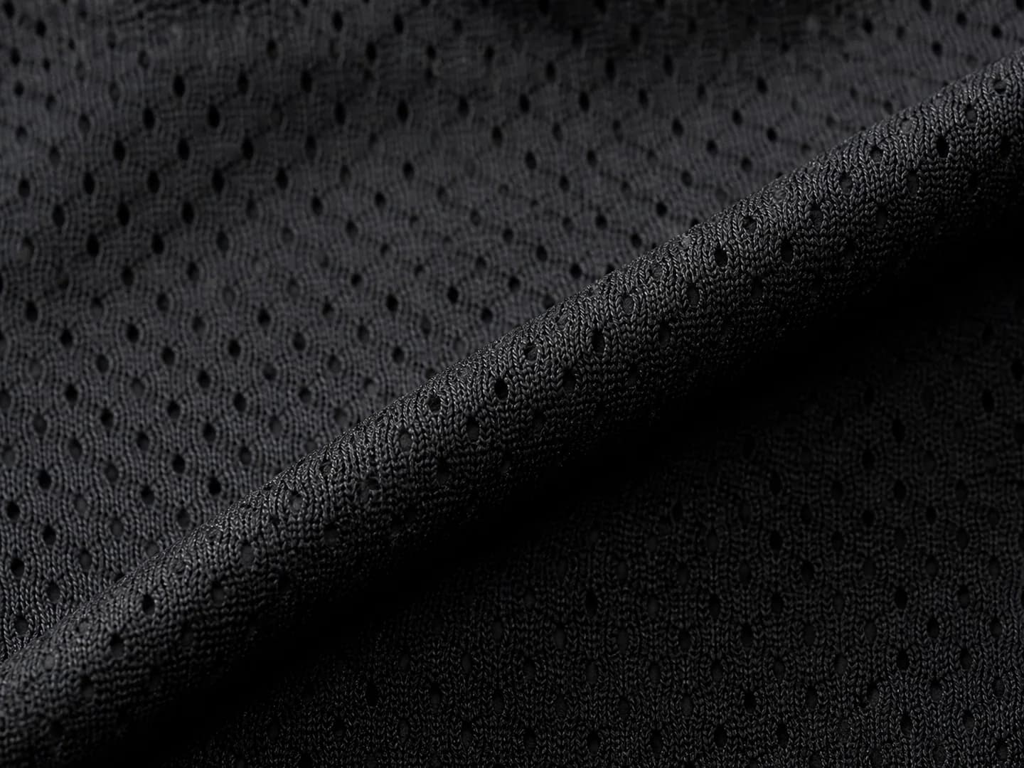 Macro view of black moisture-wicking basketball mesh with open perforations