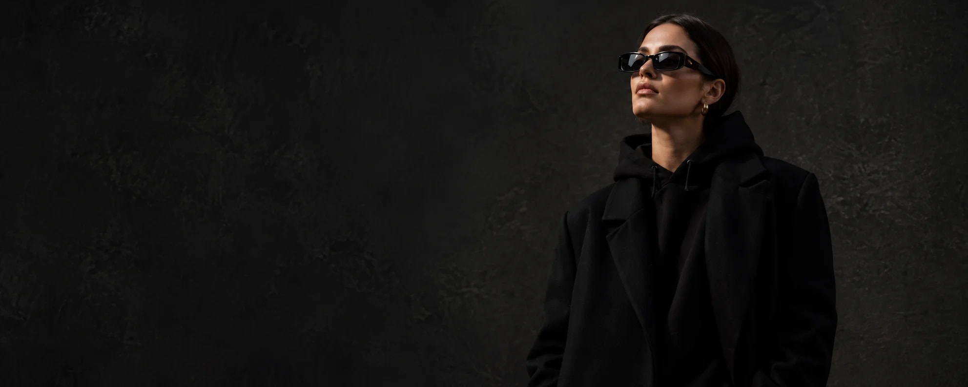 Woman in sunglasses wearing a black pullover hoodie under a black coat