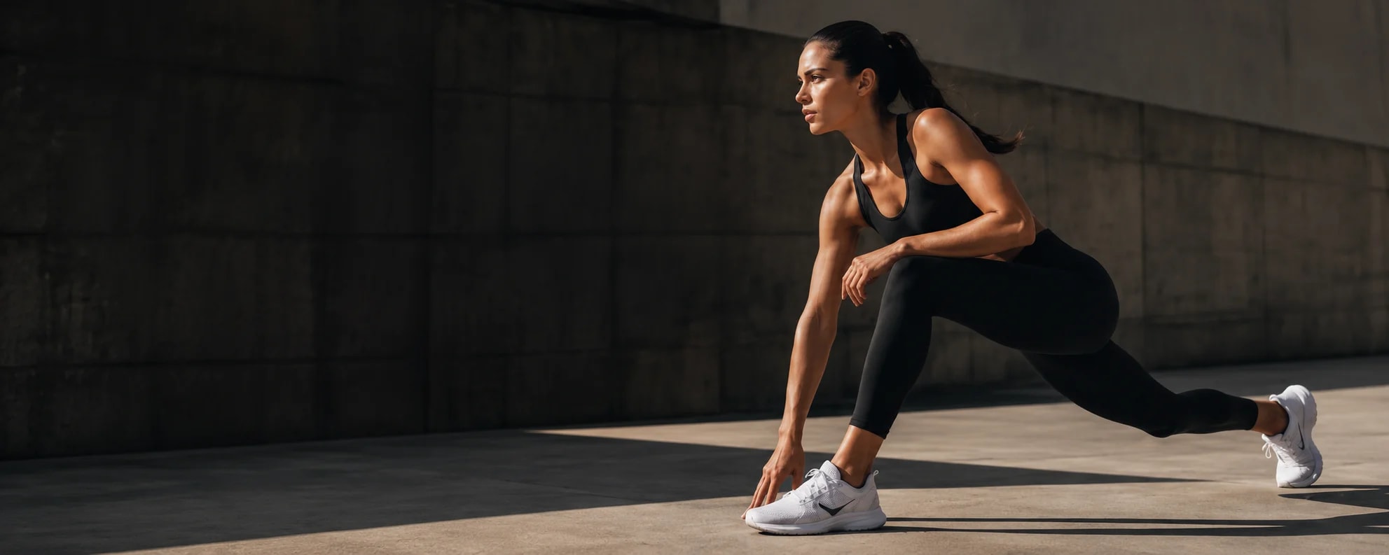 Woman stretching in a lunge wearing a black athletic top and leggings with white trainers